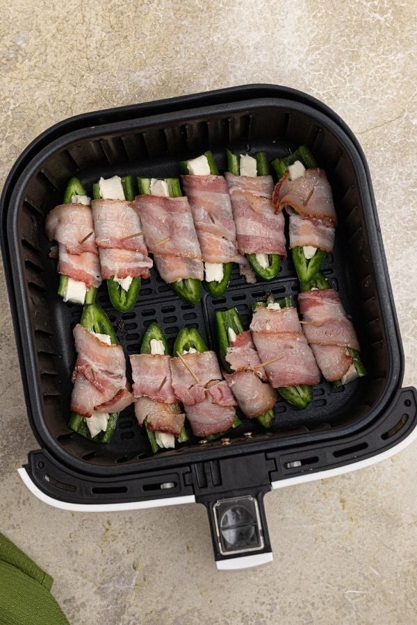 Uncooked Jalapeños wrapped in bacon in the air fryer basket.