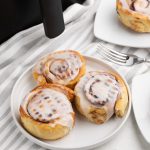 Pillsbury Cinnamon Rolls made in the air fryer ond served on a white plate.