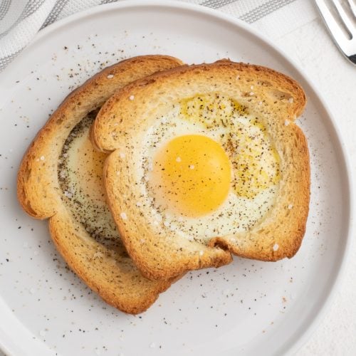 Eggs in a basket made in the Air Fryer and served on a white plate, sprinkled with salt and pepper.