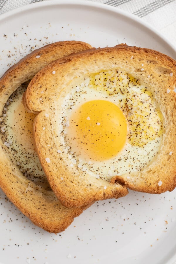 Eggs in a basket made in the Air Fryer and served on a white plate, sprinkled with salt and pepper.