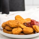 Air Fryer Frozen Chicken Nuggets on a white plate with ketchup dipping sauce.