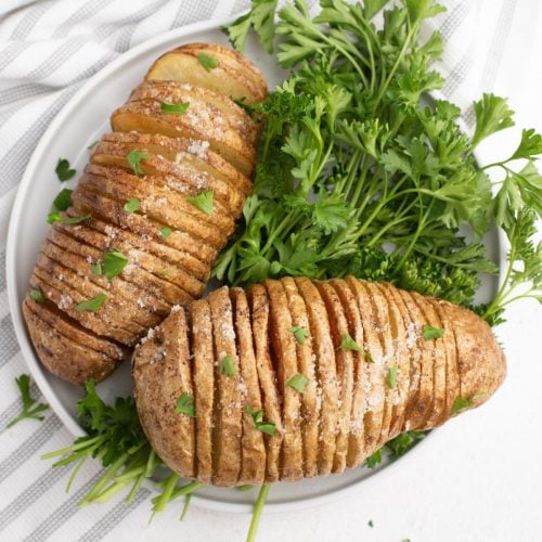 Close up sliced potatoes on a white plate with parsley garnish