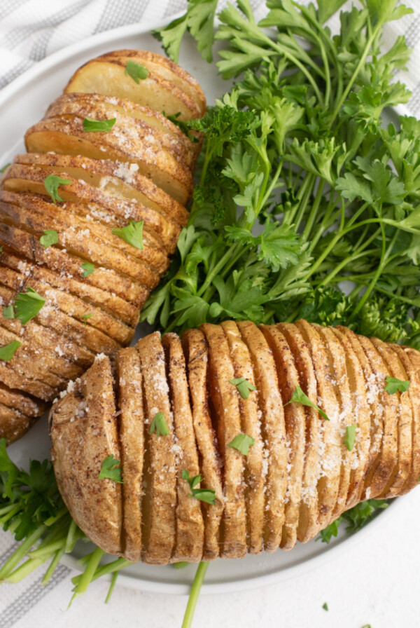 Close up sliced potatoes on a white plate with parsley garnish