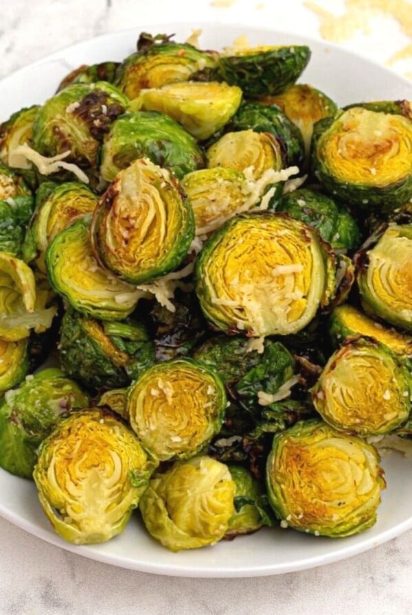 Bright green and crispy brussel sprouts on a white plate sprinkled with parmesan cheese