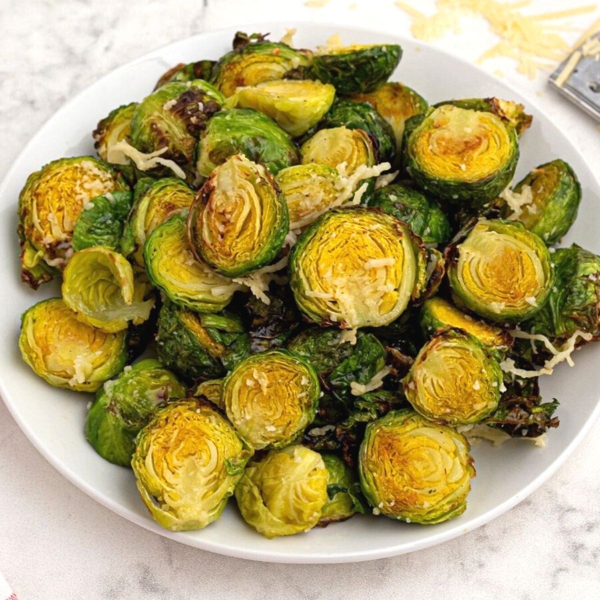 Bright green and crispy brussel sprouts on a white plate sprinkled with parmesan cheese