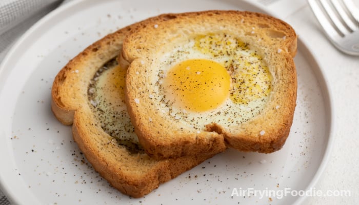 White toast with fried egg cooked on top, served on a white plate. 