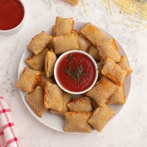 Cooked pizza rolls cooked and served on a white plate with shredded parmesan cheese and red dipping sauce.