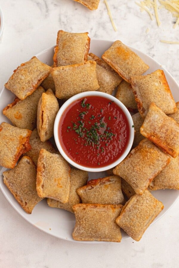 Cooked pizza rolls cooked and served on a white plate with shredded parmesan cheese and red dipping sauce.