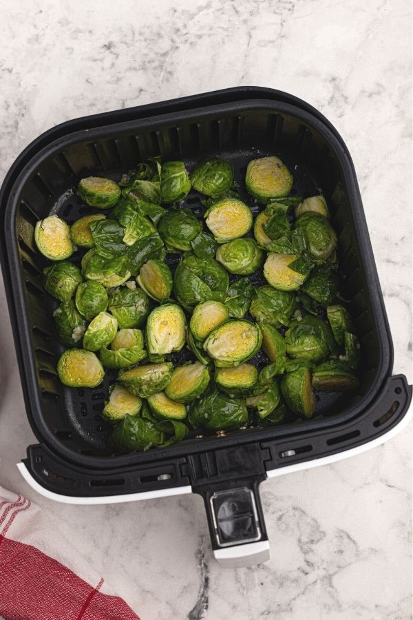 Uncooked cut brussel sprouts, tossed in olive oil and crushed garlic, spread out in the air fryer basket. 