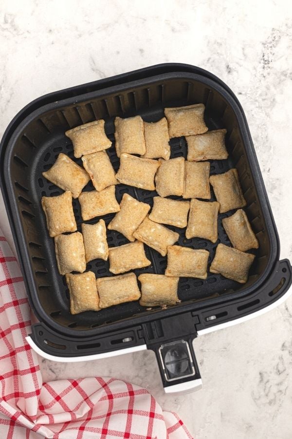 Frozen uncooked bites spread out in the air fryer basket. 