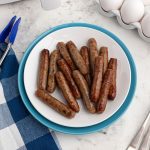 Cooked sausage links on a white plate with eggs and air fryer on the table.