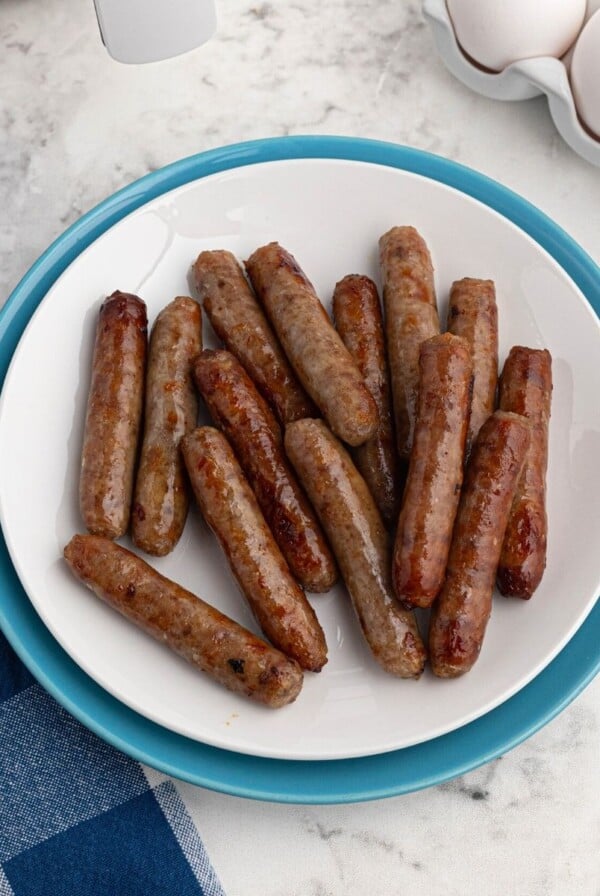 Cooked sausage links on a white plate with eggs and air fryer on the table.