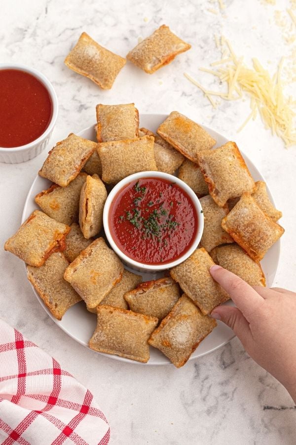 Cooked rolls served on a white plate with red dipping sauce and grated cheese on the table. 