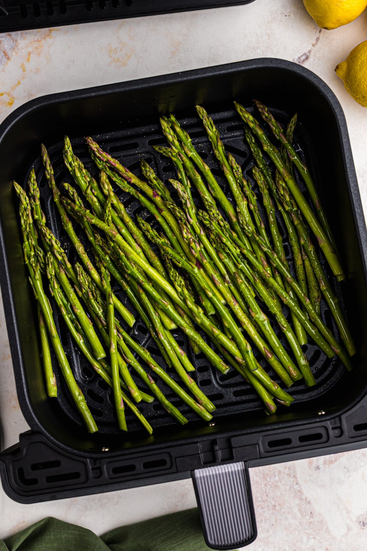 Asparagus in the air fryer basket after being seasoned and before being cooked