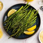 Juicy asparagus topped with parmesan cheese and lemon wedges on a blue plate