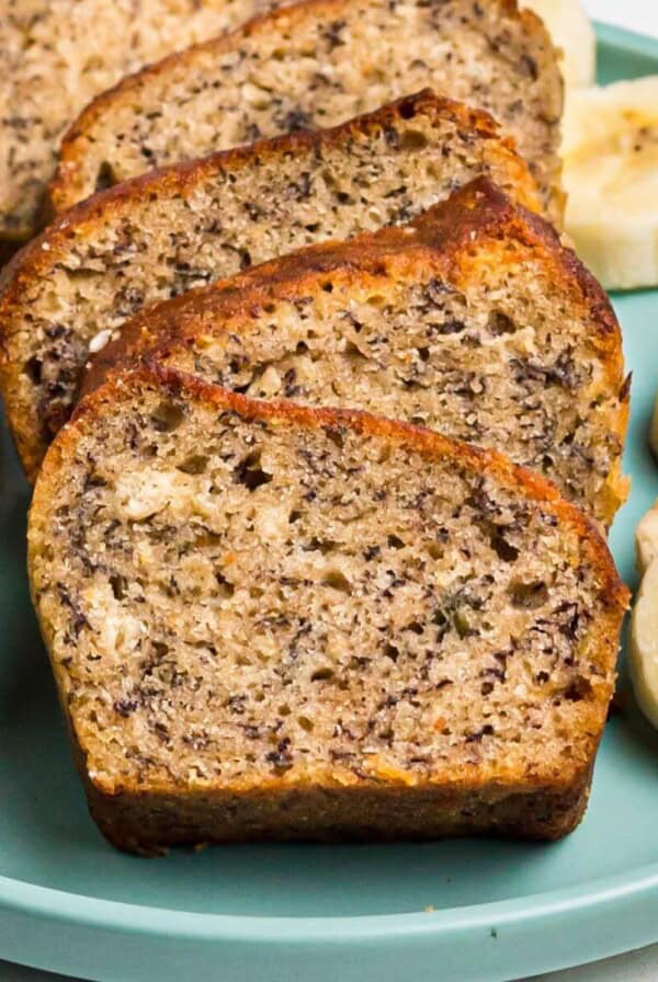 Golden moist bread sliced on a light green plate with slices of bananas.