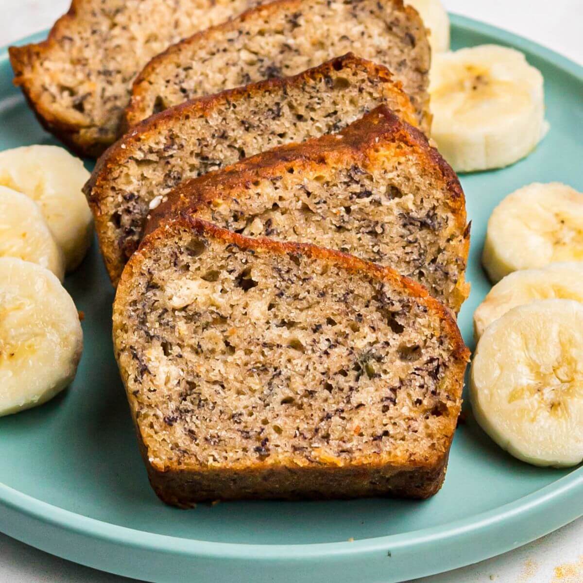 Golden moist bread sliced on a light green plate with slices of bananas.