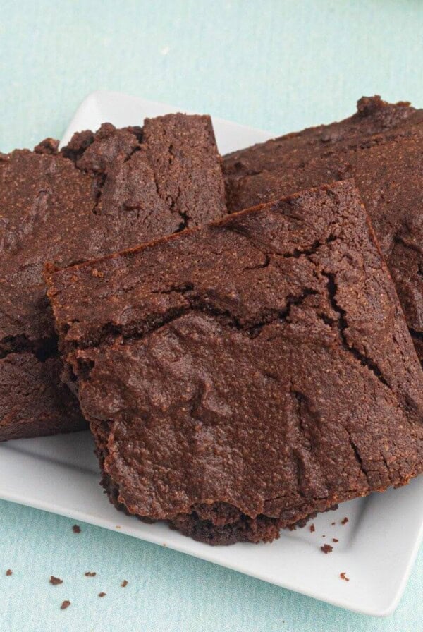 Chocolate brownies stacked on a white plate in front of an air fryer.