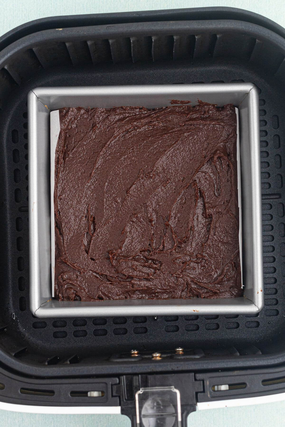 Brownie batter in a square pan in the air fryer basket before being cooked. 