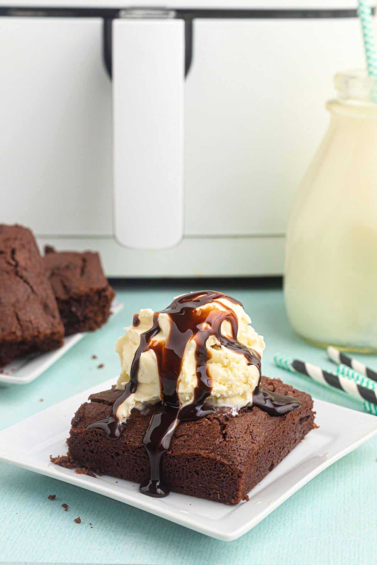 Chocolate brownie on a white square plate, topped with a scoop of ice cream and a drizzle of chocolate sauce. 