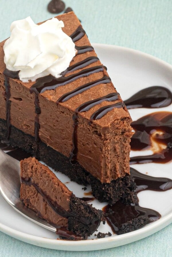 Air Fryer Chocolate Cheesecake served on a white plate with a bite on the fork next to it. Drizzled with melted chocolate.