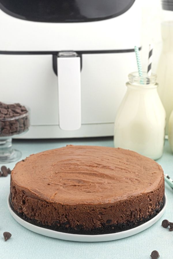 Full chocolate cheesecake, served on a white late, before being sliced, in front of the air fryer. 