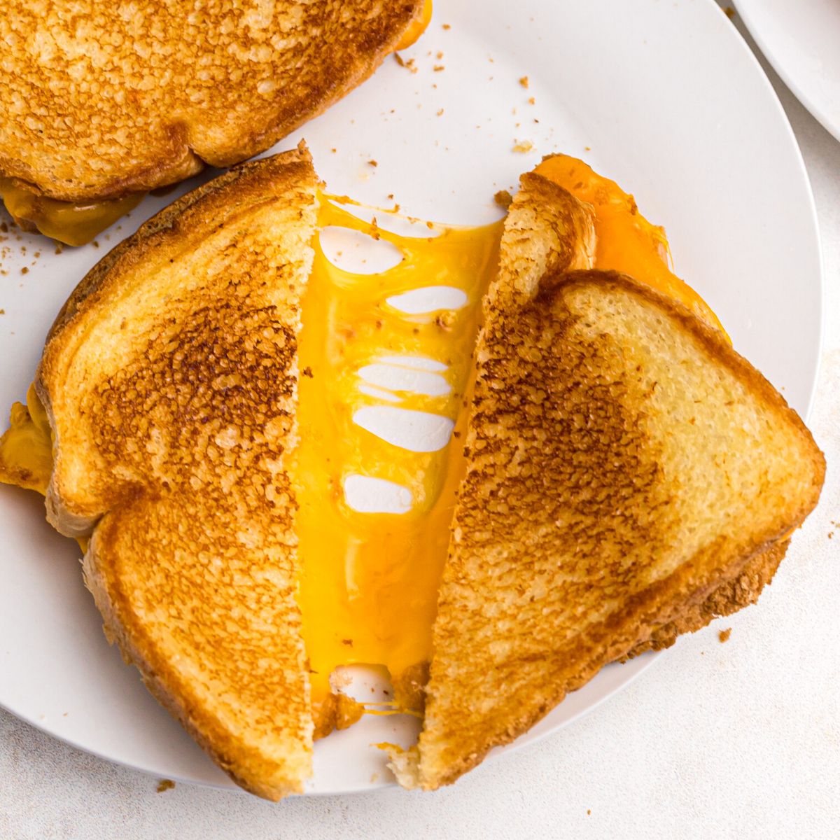 Golden crispy grilled cheese sandwich sliced in half with melty cheese coming out.