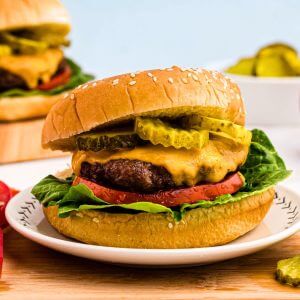 Juicy hamburger topped with cheese, lettuce, tomato and pickles, on a bun.