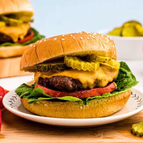 Juicy hamburger topped with cheese, lettuce, tomato and pickles, on a bun.