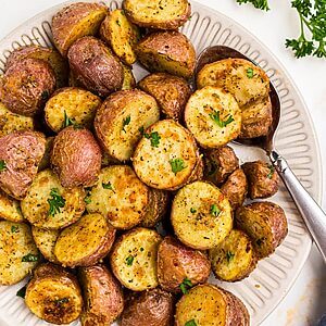 Golden crispy seasoned baby potatoes on a white plate with a serving spoon in the corner of the plate.