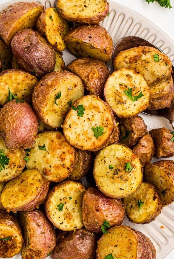 Golden crispy seasoned baby potatoes on a white plate with a serving spoon in the corner of the plate.