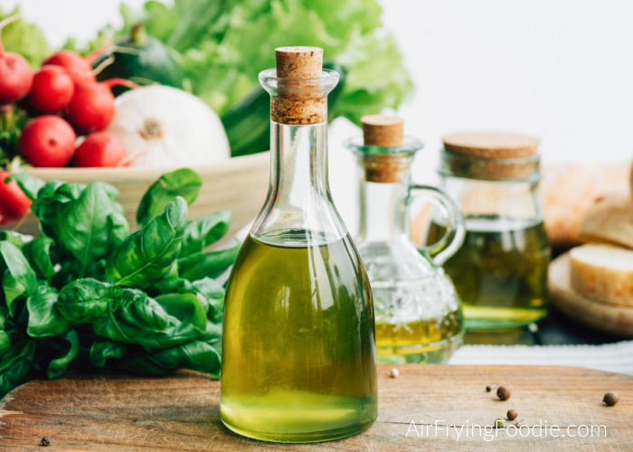 To answer questions about which bottle of oil  to use in an air fryer, a photo of oil, with vegetables in a bowl in the background