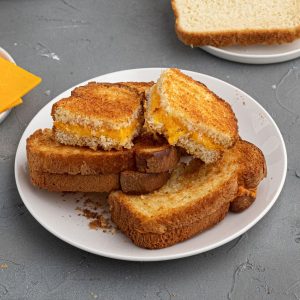Cooked, golden crispy grilled cheese sandwich cut and served onto a white plate.