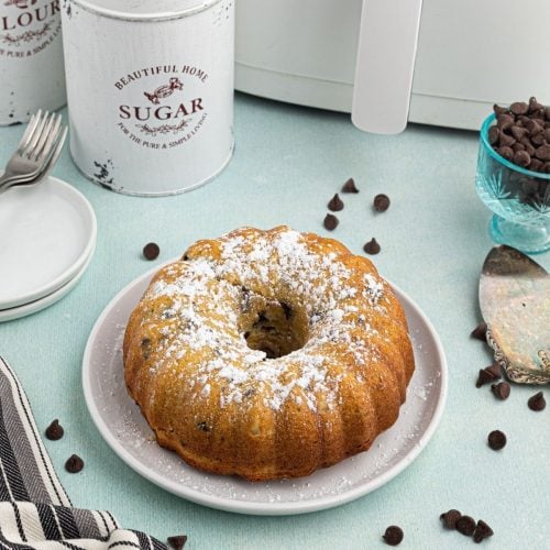 Round golden Bundt cake with chocolate chips scattered and in front of the air fryer.