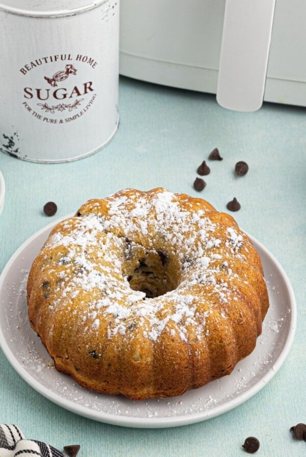 Round golden Bundt cake with chocolate chips scattered and in front of the air fryer.