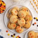 Baked sugar cookies scattered on a white plate, with Reece's Pieces candy scattered around the plate.