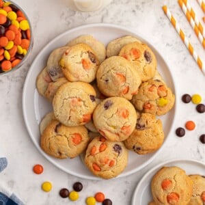 Baked sugar cookies scattered on a white plate, with Reece's Pieces candy scattered around the plate.