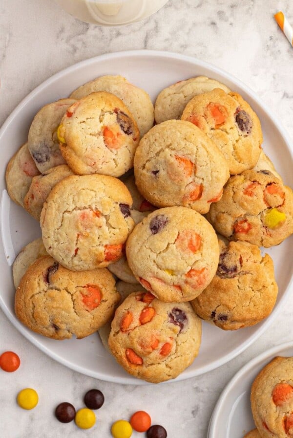 Baked sugar cookies scattered on a white plate, with Reece's Pieces candy scattered around the plate.