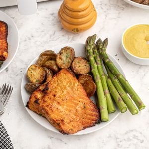 Cooked honey mustard glazed salmon served on a white plate with asparagus.