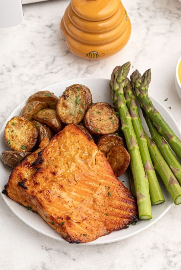 Cooked honey mustard glazed salmon served on a white plate with asparagus.