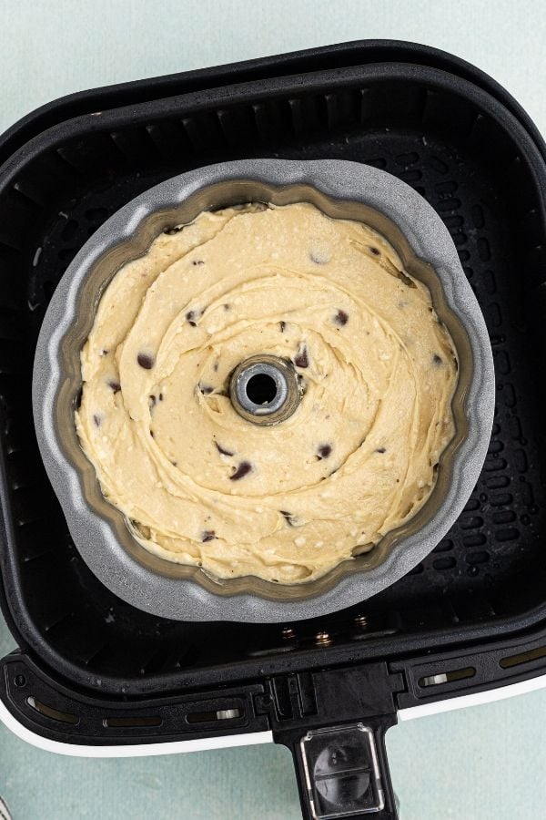 Uncooked raw pound cake dough in a bundt cake pan set in an air fryer basket. 