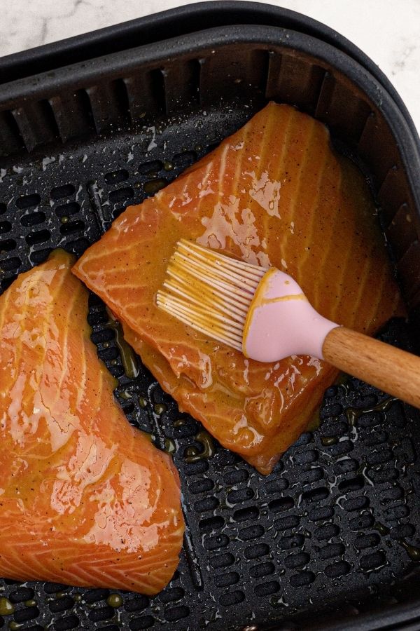 Uncooked salmon in the air fryer basket, being brushed with the honey mustard glaze. 
