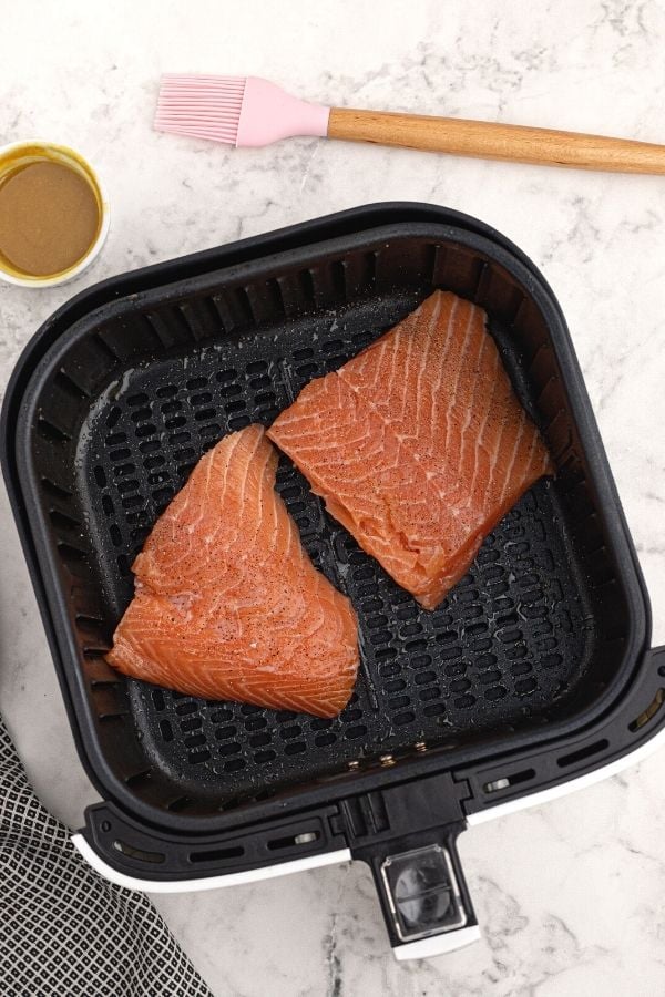 Un cooked salmon, seasoned, in the air fryer basket. 