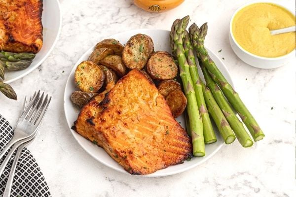 Crispy and golden salmon with a honey  mustard glaze, served on a white plate with asparagus and potatoes. 
