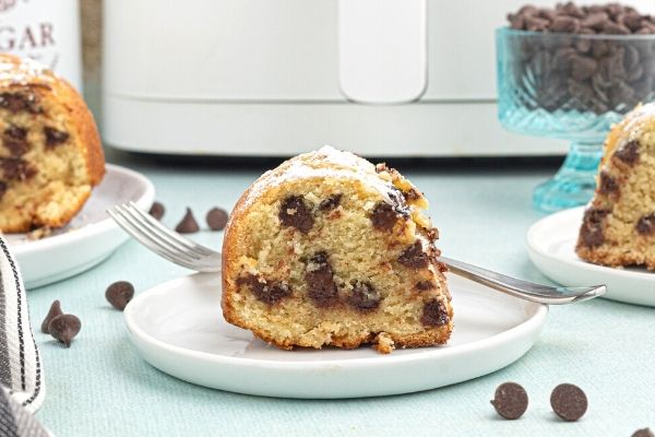 Cut slice of chocolate chip pound cake, served on a white plate, cooked in the air fryer with chocolate chips scattered around the table. 