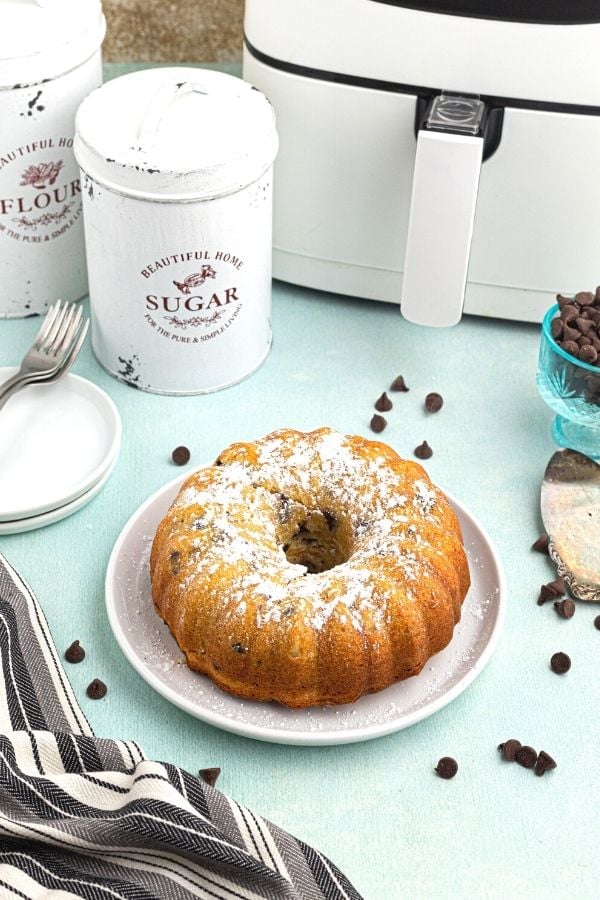 Baked pound cake served on a white plate, whole, sprinkled with powdered sugar and chocolate chips scattered around the plater. 