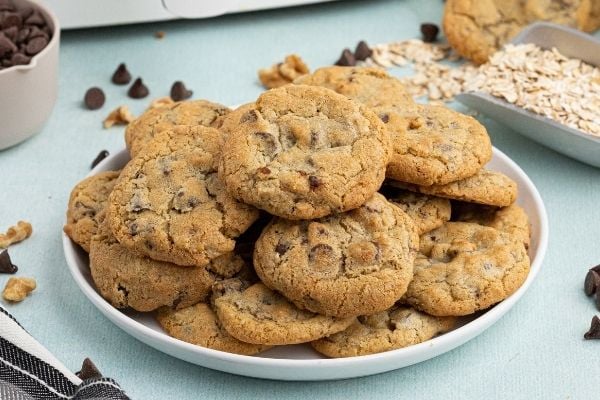 Golden chocolate chip cookies on a white plate with oats and chocolate chips scattered. 