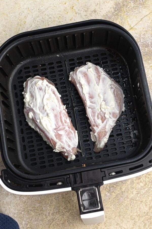 Uncooked chicken in the air fryer basket, covered with yogurt. 