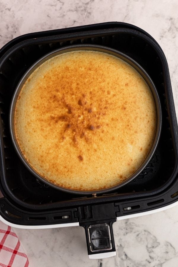 Cooked cheesecake in a pan, placed inside the basket of an air fryer. 
