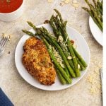 Cooked parmesan crusted chicken served with green asparagus on a white plate.